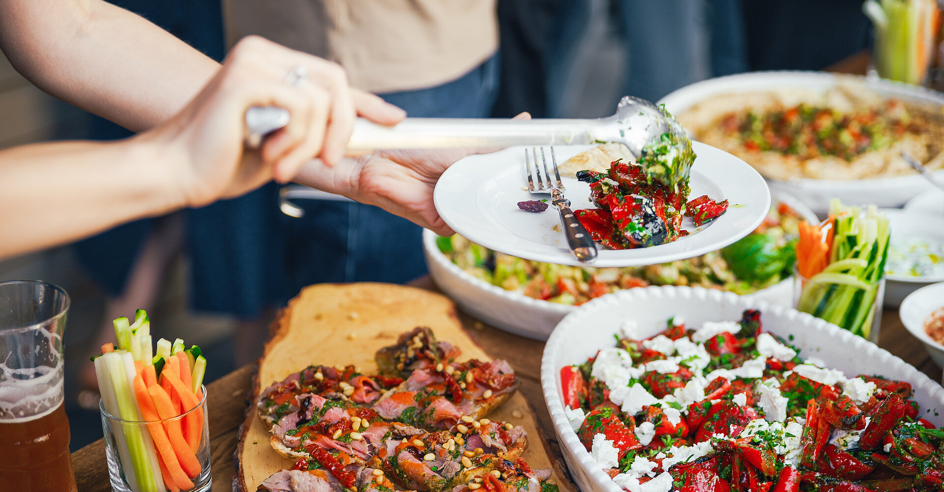 Frauenhand stapeln sich eine Mahlzeit in einen Teller mit Mittagessen. Das Konzept der Ernährung. Buffet. Essen. Abendessen. Das Konzept des Teilens.