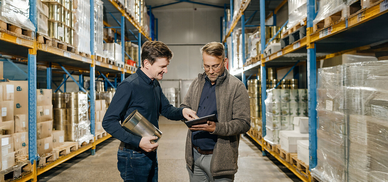 Two employees are standing between the high-rack storage areas, discussing inventory levels