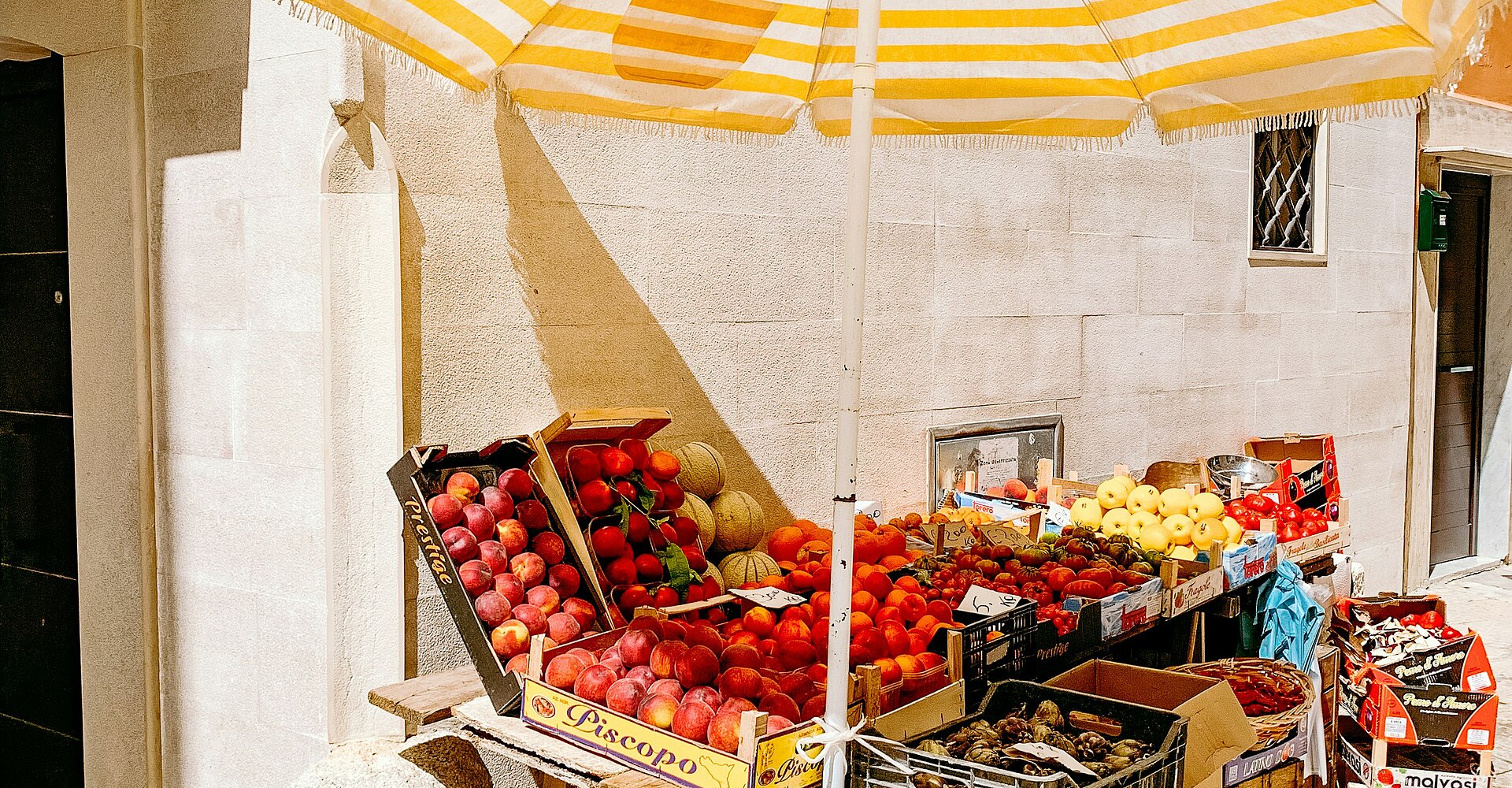 ein gelb-weißer Regenschirm und einige Kisten mit Früchten