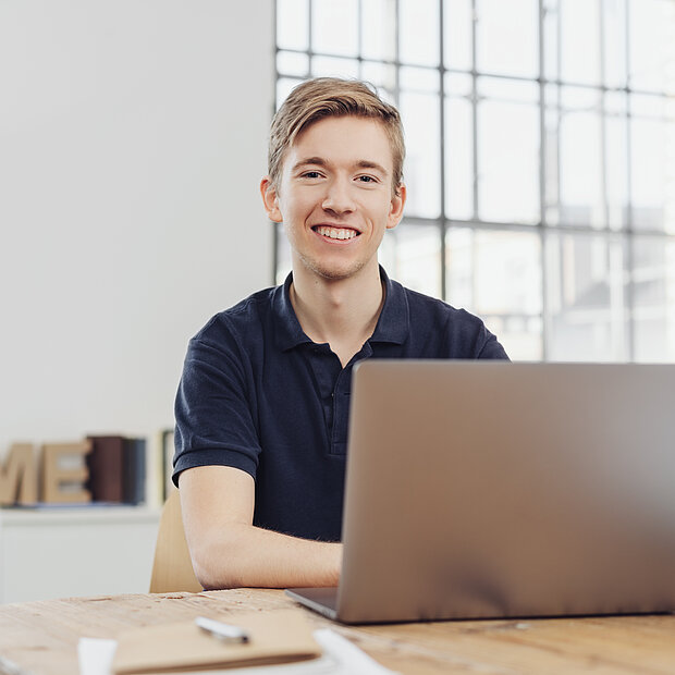 Junger fröhlicher Mann sitzt vor Laptop