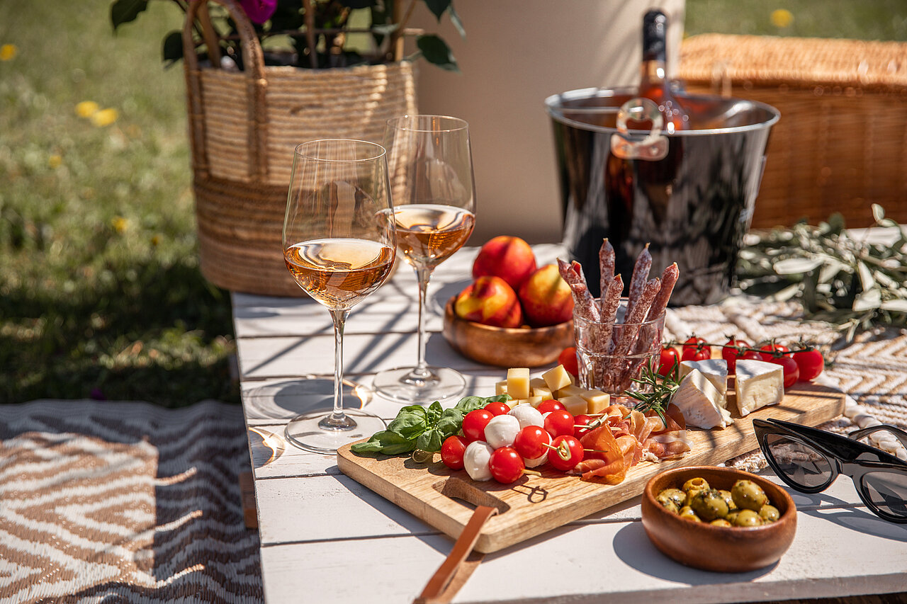 Rosé wine glasses with antipasti and picnic snacks on a sunny garden party table